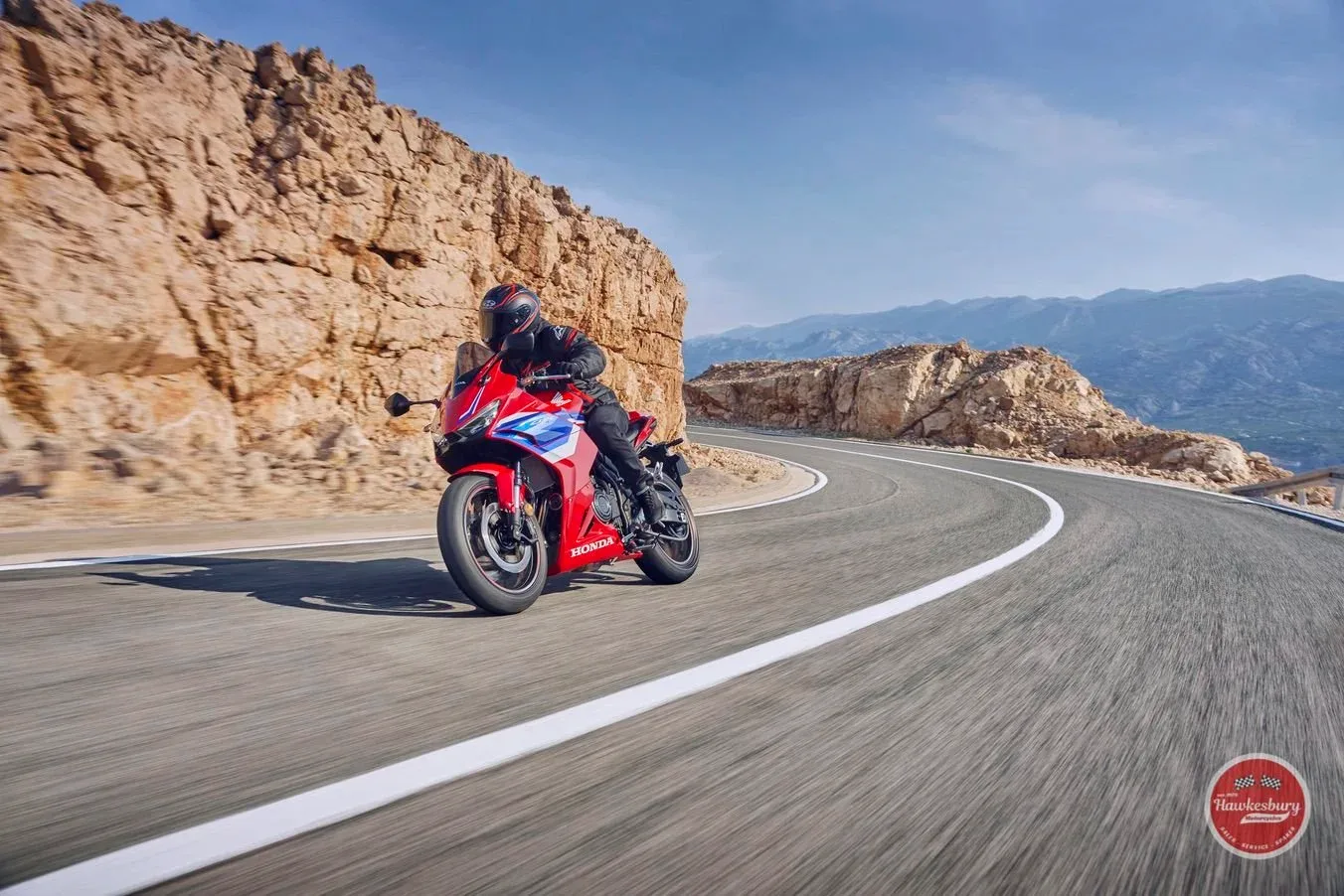 Rider on a Honda CBR500R on a winding mountain road with rocky cliffs behind