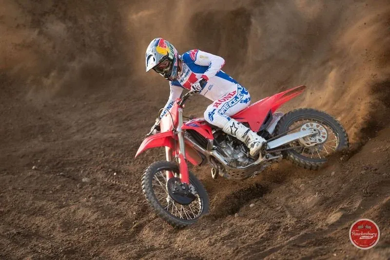 A rider in white, blue and red gear riding a red Honda CRF250R on a dirt track
