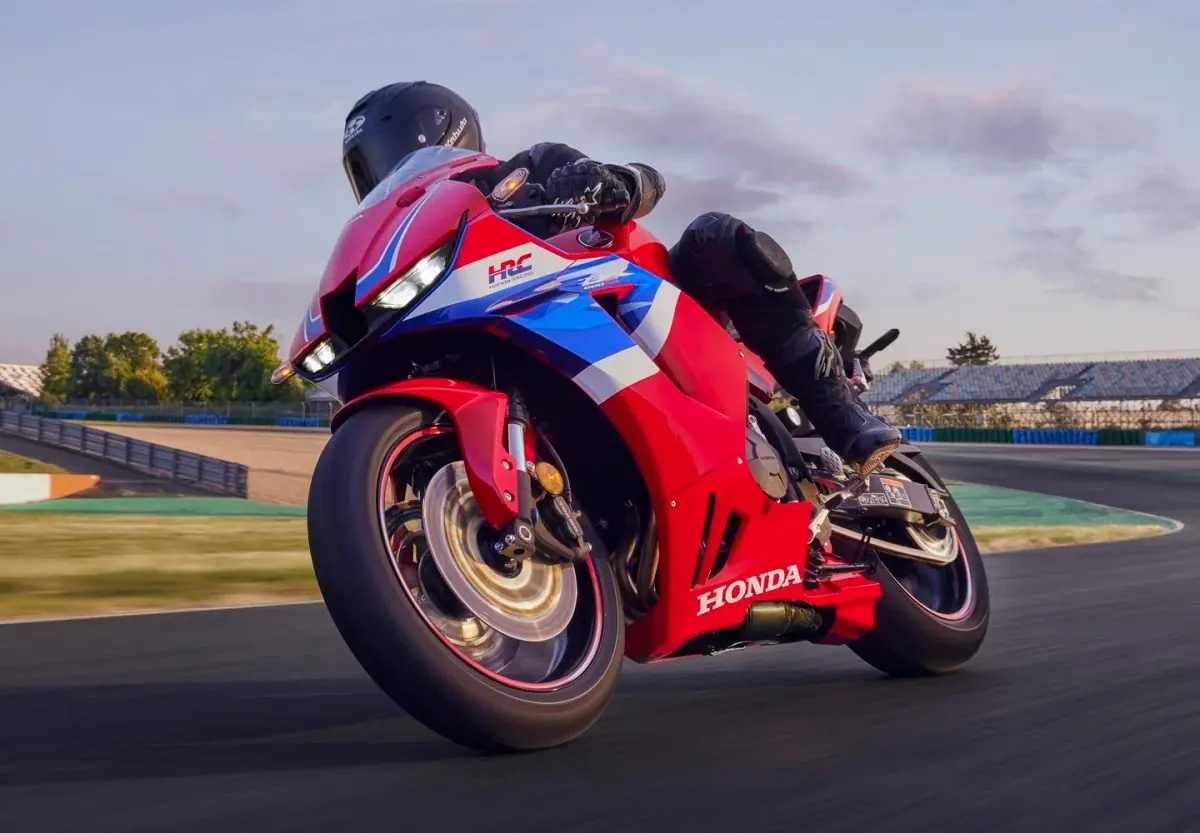 A red, blue and white Honda CBR600RR racing motorcycle mid-turn on a race track, the rider in black protective gear leaning into the curve