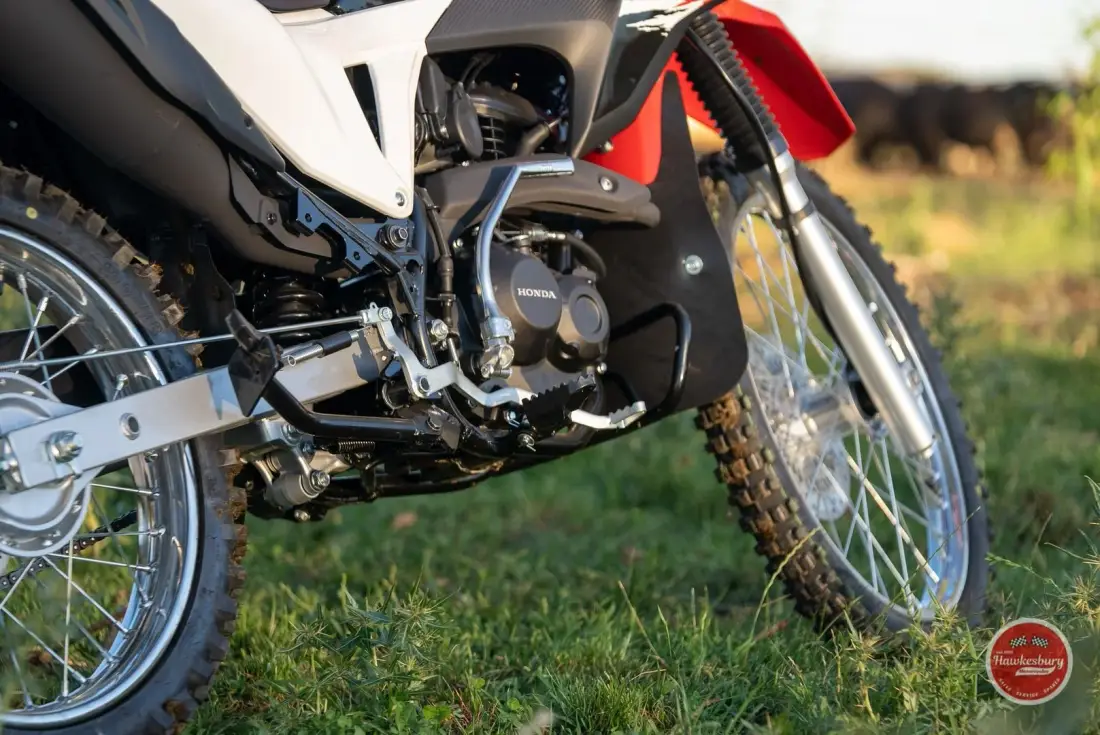 Close-up of a Honda XR190CT engine, frame and front wheel, with a bash plate fitted and grass underneath