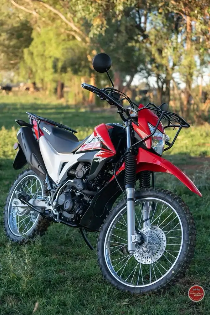 Red Honda XR190CT farm bike with front and rear carry racks, standing in a grassy paddock at dusk with trees behind